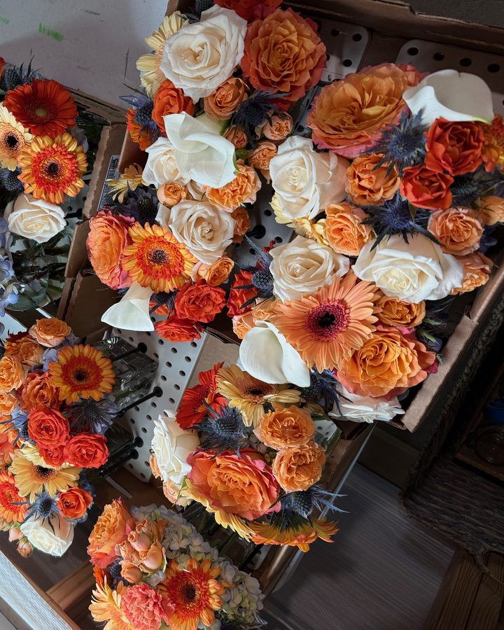 A spread of custom event bouquets in burnt orange, cream, and blue with roses, gerbera daisies, and thistle